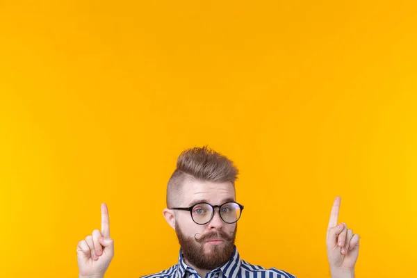 Solution is here. Handsome funny young man pointing copy space and looking at camera while standing against yellow background
