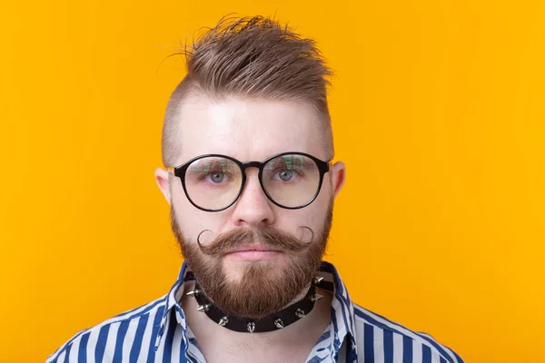 Joven hombre de moda positivo hipster con una barba bigote y collar fetiche en camisa posando sobre un fondo amarillo. Concepto de roca y subcultura . — Foto de Stock