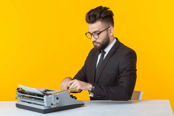 Hombre de negocios o gerente árabe en traje formal escribiendo texto en una máquina de escribir sobre un fondo amarillo. Concepto de trabajo empresarial y de oficina —  Fotos de Stock