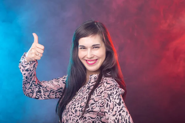 Sonriente mujer joven bonita mostrando el pulgar hacia arriba en el fondo colorido — Foto de Stock