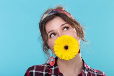 Retro görüntü komik pozitif genç kadın mavi bir arka plan karşı poz dişlerinde parlak sarı gerbera çiçek tutan. Sürpriz ve eğlence kavramı.
