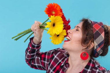 Ekose gömlek ve mavi bir arka plan üzerinde poz güzel parlak gerbera çiçekler koklama bir bandaj güzel pozitif genç kadın. Hediye ve selam kavramı.