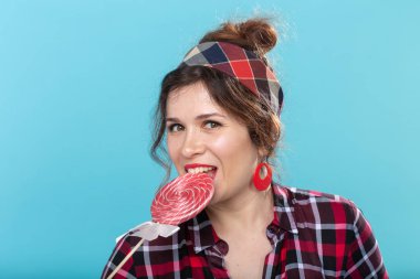 Mavi arka plan üzerinde lolipop yiyen güzel genç kadının portresini kapatın