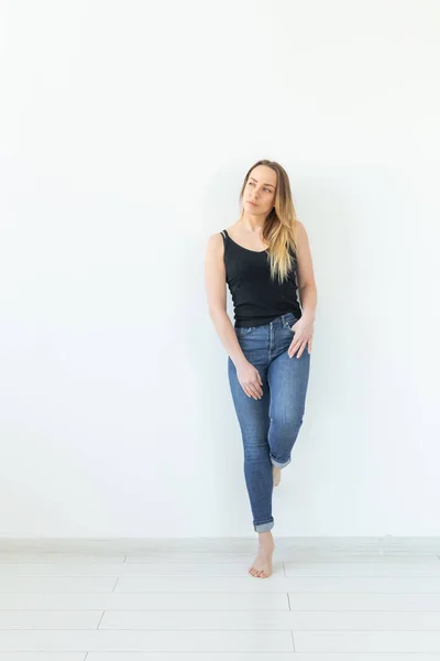 风格和人的概念 - 年轻女子在牛仔裤站在白色的墙壁，看起来像性感 — 图库照片