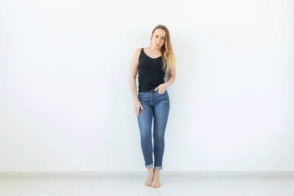 Estilo e conceito de pessoas - jovem mulher de jeans em pé sobre a parede branca e parece sexy — Fotografia de Stock