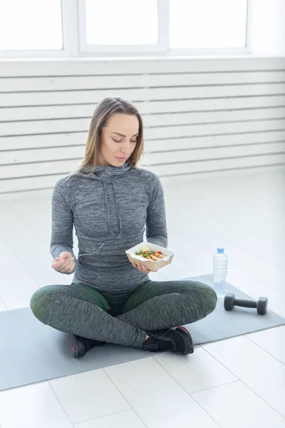 sport, healthy, people concept - Girl holding salad and dumbbell after fitness training