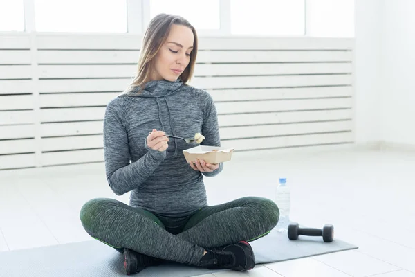 Deporte, estilo de vida saludable, concepto de personas - Mujer rubia joven en ropa de fitness, con comida vegetariana saludable, sentado en el suelo — Foto de Stock