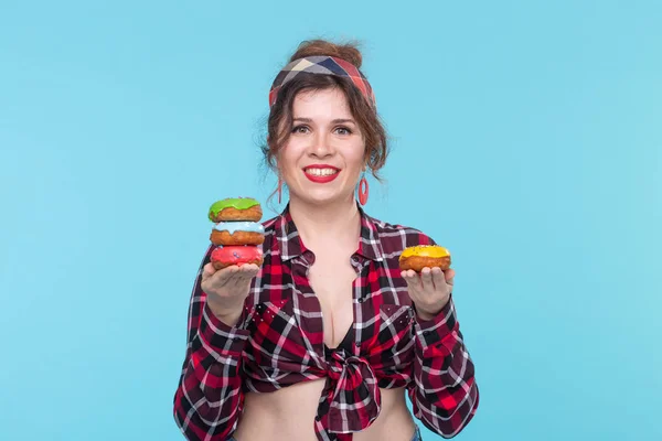 손에 들고 긍정적 인 젊은 핀 업 소녀 모델은 파란색 배경에 포즈 네 개의 여러 가지 빛깔의 도넛을 들고. 디저트와 과자를 위한 요리 컨셉. — 스톡 사진
