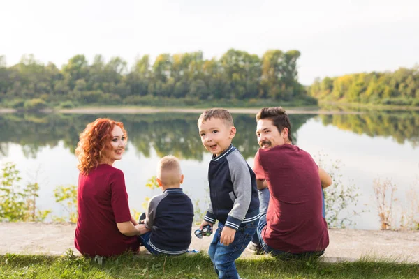 La paternidad, la naturaleza, el concepto de la gente - familia con dos hijos sentados cerca del lago — Foto de Stock