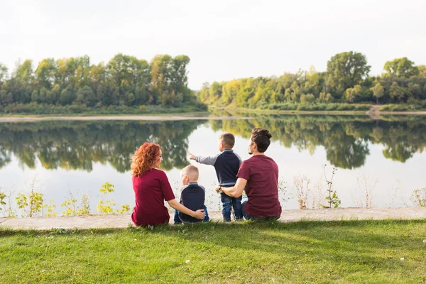 Parenthood, nature, people concept - family with two sons sitting near the lake — Stock Photo, Image