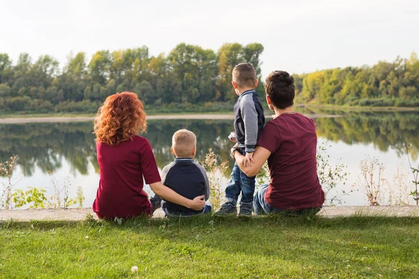 Föräldraskap, natur, människor koncept - familj med två söner sitter nära sjön — Stockfoto