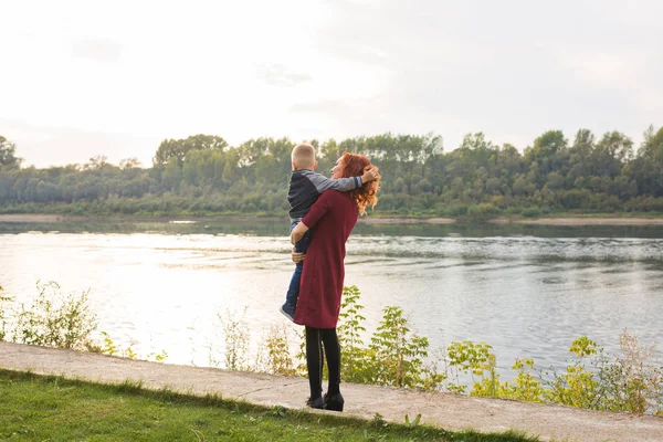 Mutterschafts- und Kinderkonzept - junge Mutter mit Sohn im Arm in der Nähe des Flusses — Stockfoto