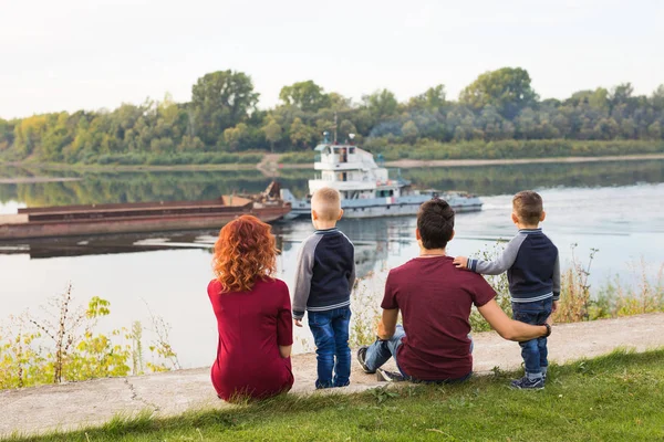 Föräldraskap, barndom och natur koncept - familjen sitter på den gröna marken och tittar på liten båt — Stockfoto