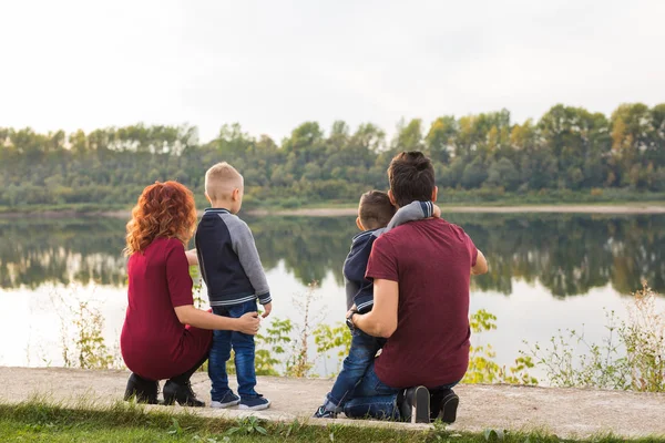 Parenthood, childhood and family concept - Parents and two male children walking at the park and looking on something, back view — Stock Photo, Image