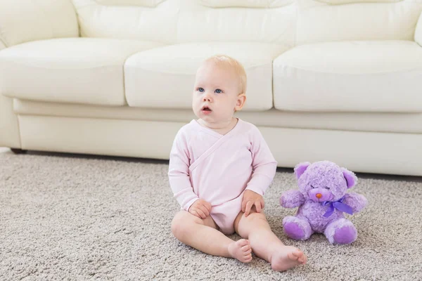 Liten krypande bebis flicka ett år gammal sitter på golvet i ljust ljus vardagsrum leende och skrattar. Happy småbarn Kid spelar hemma. Barndoms konceptet — Stockfoto