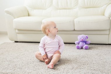 Küçük emekleme kız kız bir yaşında parlak ışık oturma odasında katta gülümseyerek ve gülüyor oturuyor. Evde oynayan mutlu bir çocuk. Çocukluk kavramı