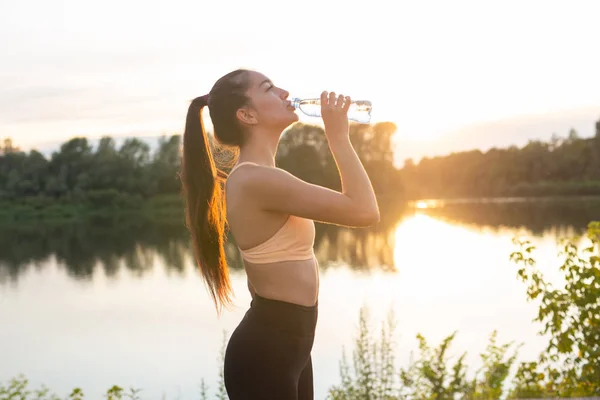 Fitness, outdoor training and people concept - Young woman drinking water after jogging