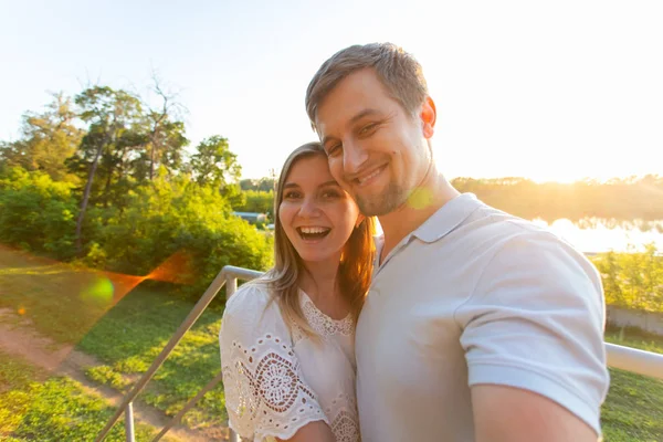 Casal romântico engraçado bonito no fundo da natureza. Jovem atraente e homem bonito estão fazendo selfie, sorrindo e olhando para a câmera . — Fotografia de Stock