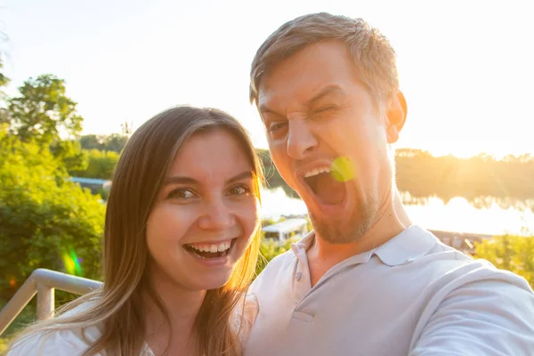 Beautiful funny romantic couple on nature background. Attractive young woman and handsome man are making selfie, smiling and looking at camera. — Stock Photo, Image