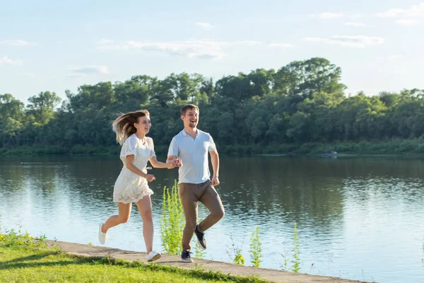 Liebes- und Beziehungskonzept - der glückliche Mann und die glückliche Frau beim Laufen in einem Park am See — Stockfoto