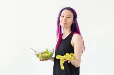 Renkli saçlı ince genç asya kız bir ölçüm bandı tutar ve elinde beyaz bir arka plan üzerinde poz hafif bir sebze salatası tutan. Sağlıklı beslenme konsepti. Copyspace.