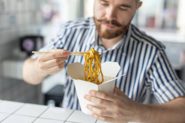 Pozitif genç şık adam iş yerinde bir mola sırasında bir kafede Çin erişte yemek. Dinlenme ve sağlıklı atıştırmalık kavramı.