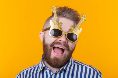 Gitar şeklinde gözlüklü pozitif genç adam sarı bir arka plan karşı sevinir. Kutlama ve partiler kavramı.