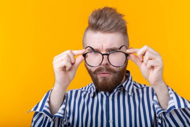 Sarı bir arka planda ayakta iken genç yakışıklı adam gözlüklerini bakıyor. Kötü vizyon ve göz tedavisi kavramı.