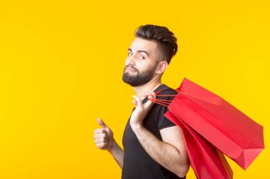 Adam sarı bir arka planda kırmızı alışveriş torbaları tutuyor. Süpermarket ve hediyeler alışveriş kavramı. Reklam alanı.