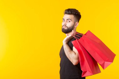 Adam sarı bir arka planda kırmızı alışveriş torbaları tutuyor. Süpermarket ve hediyeler alışveriş kavramı. Reklam alanı.