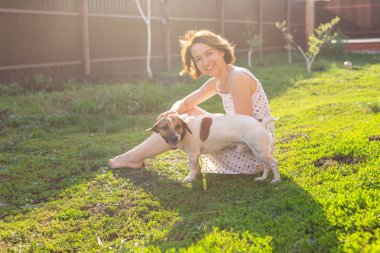 Elbise içinde Gülen pozitif genç kadın güneşli bir yaz gününde bir kır evinin bahçesinde oturan sevgili huzursuz köpek ile oynar. Aile hafta sonu konsepti.