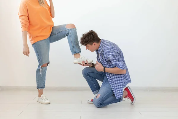 El joven se arrodilla y con reverencia ata los cordones de los zapatos a su dominante mujer no identificada posando sobre un fondo blanco. Concepto de relaciones dominantes . —  Fotos de Stock