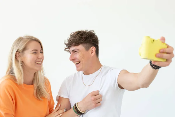 Lustiges verrücktes junges Paar blondes Mädchen und ein Hipster-Typ, die ein Selfie auf einer gelben Vintage-Filmkamera auf weißem Hintergrund machen. Konzept der Fotografie Hobby. — Stockfoto