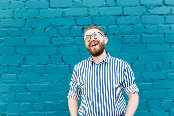 Retrato de estudante elegante positivo alegre em copos com um bigode e barba posando contra uma parede azul. O conceito de pessoas alegres bem sucedidas. Espaço de cópia — Fotografia de Stock