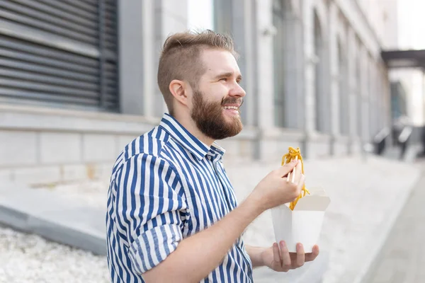 Zblízka na zábavného mladého hipstera, který jedl čínské nudle s dřevěnými hůlky sedících v parku venku za teplého letního dne. Koncept odpočinku a zachvívání na ulici. — Stock fotografie