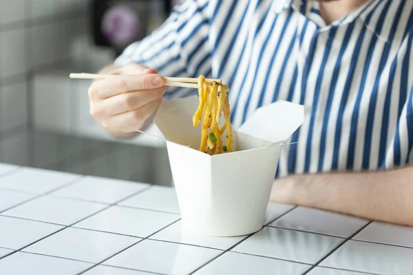 Close-up de um jovem homem não identificado mão em uma camisa estão segurando paus de madeira macarrão chinês. Delicioso asiático conceito de cozinha . — Fotografia de Stock