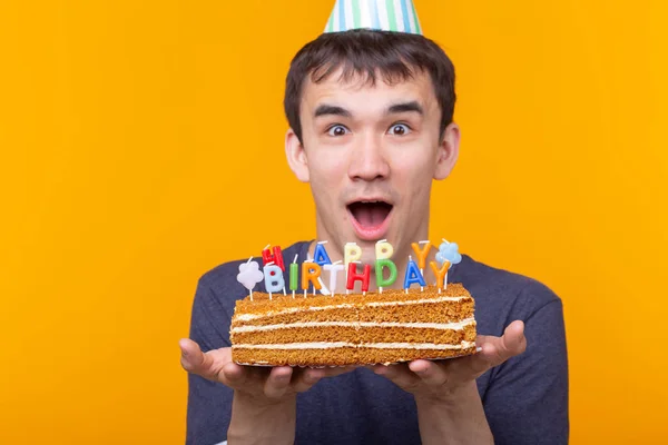 Crazy vidám fiatal ázsiai fickó szemüveg kezében égő gyertyát a kezében, és egy gratuláló házi torta a sárga háttér. Születésnapi és évforduló ünnepe koncepció. — Stock Fotó