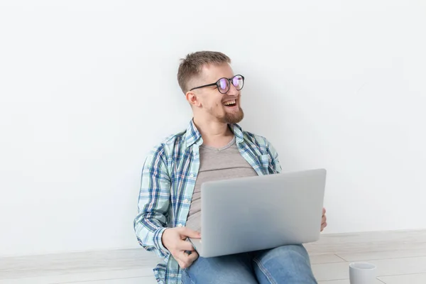 Θετικός νέος άντρας με casual ρούχα και γυαλιά να σερφάρει στο διαδίκτυο χρησιμοποιώντας Wi-Fi και ένα φορητό υπολογιστή σε αναζήτηση κατοικιών ενοικίασης. Σχέδιο οικιακής σίτισης και αναζήτησης διαμερισμάτων. — Φωτογραφία Αρχείου