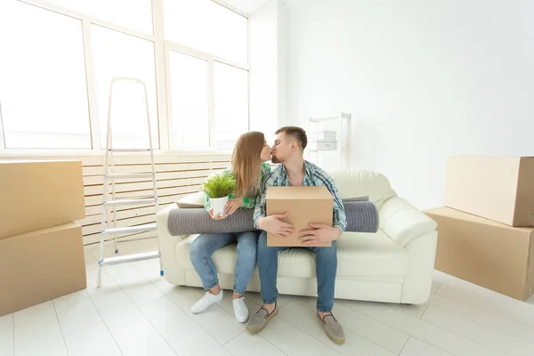 Flytta och fastigheter koncept - lyckliga paret kysser på soffa i nya lägenheten — Stockfoto
