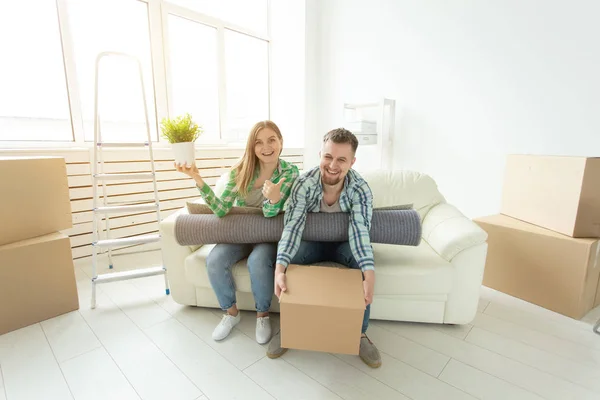 Moving, relocation and new home concept - young couple having fun on the couch surrounded with boxes