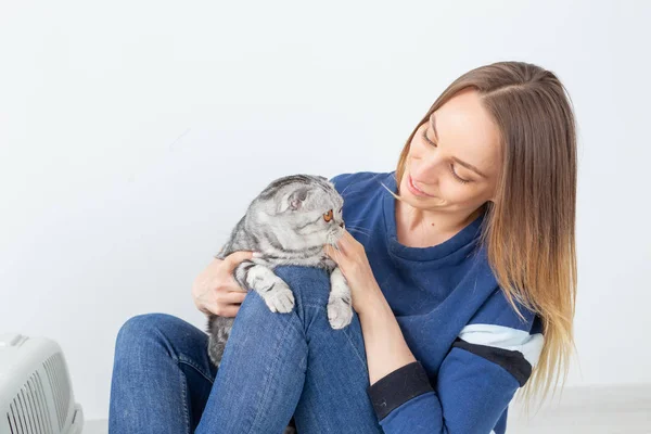 Charming positive young woman holds in her hands her beautiful gray fold scottish cat sitting on the floor in a new apartment. Pet concept. — Stock Photo, Image