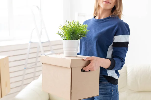 Jovem não identificada tem uma caixa e um pote de plantas enquanto se muda para um novo apartamento. Acolhimento e novo conceito de habitação . — Fotografia de Stock