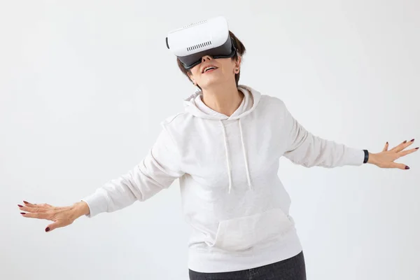 Невідома жінка середнього віку в легкому светрі грає в 3D гру з окулярами віртуальної реальності на білому тлі. Високотехнологічна концепція для літніх людей . — стокове фото