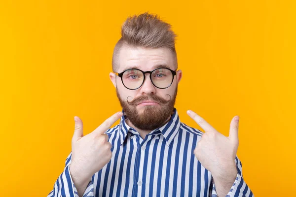 Encantador joven hombre hipster de moda con gafas y una barba se muestra posando sobre un fondo amarillo. Lugar para la publicidad. El concepto de confianza en sí mismo y éxito . — Foto de Stock