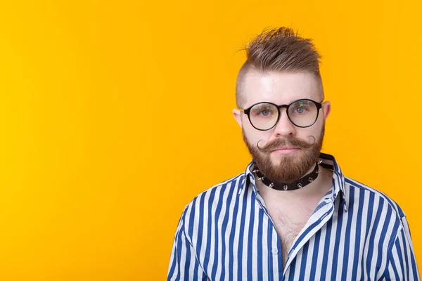 Joven hombre de moda positivo hipster con una barba bigote y collar fetiche en camisa posando sobre un fondo amarillo con espacio de copia. Concepto de roca y subcultura . — Foto de Stock