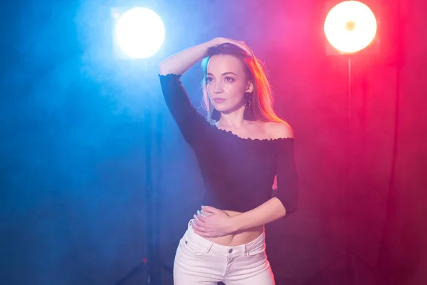 Nightlife and club concept - young woman dancing in the dark under the lights — Stock Photo, Image