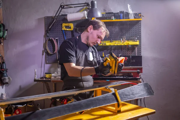 Un uomo in abiti da lavoro riparatore in officina servizio sci riparazione dello sci — Foto Stock