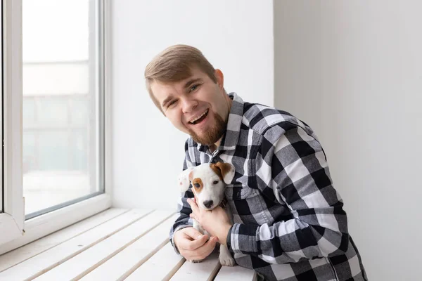 People, pets and animals concept - young man hugging jack russell terrier puppy near window on white background — Stock Photo, Image