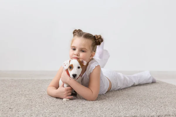people, children and pets concept - little child girl lying on the floor with cute puppy Jack Russell Terrier