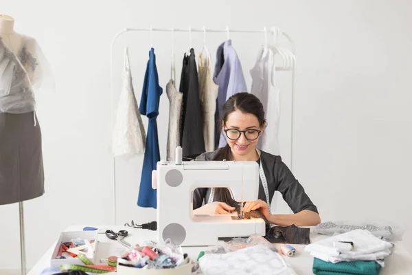 服装制造商、裁缝和时尚概念--微笑着的女性时尚设计师使用缝纫机, 坐在办公桌后 — 图库照片